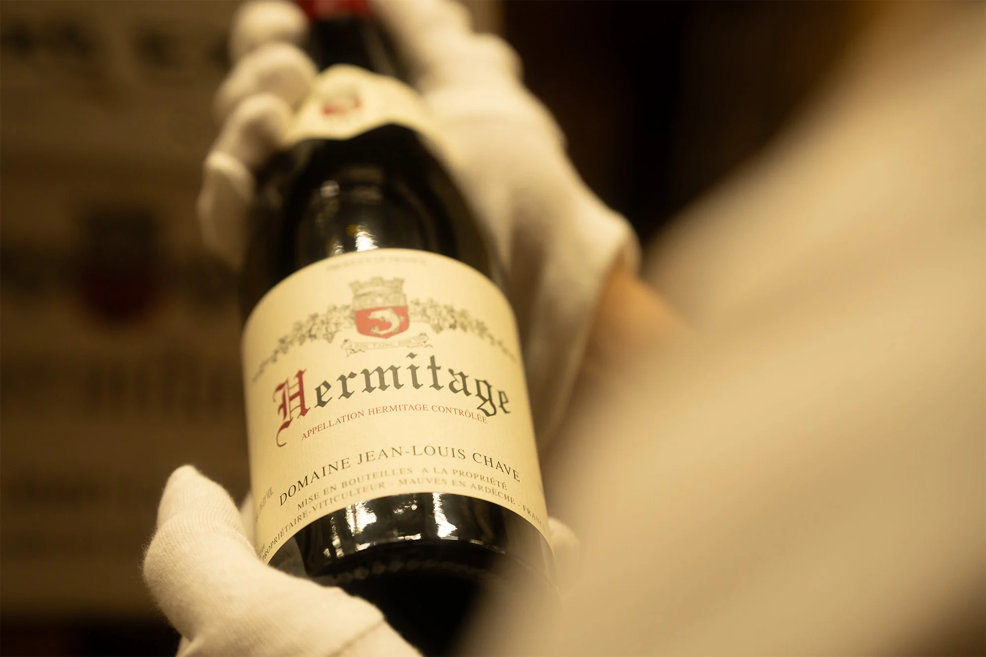 Hände in weißen Handschuhen halten eine Flasche Hermitage der Domaine Jean-Louis Chave im Weinlager